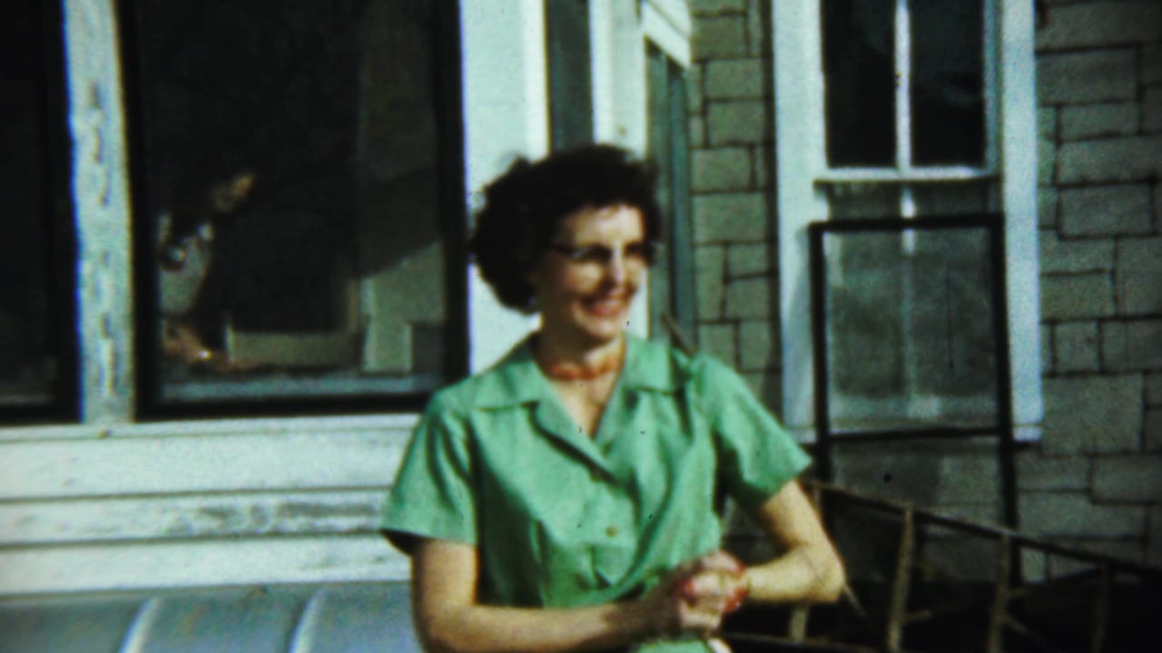 Woman in a green dress smiling beside a house window.