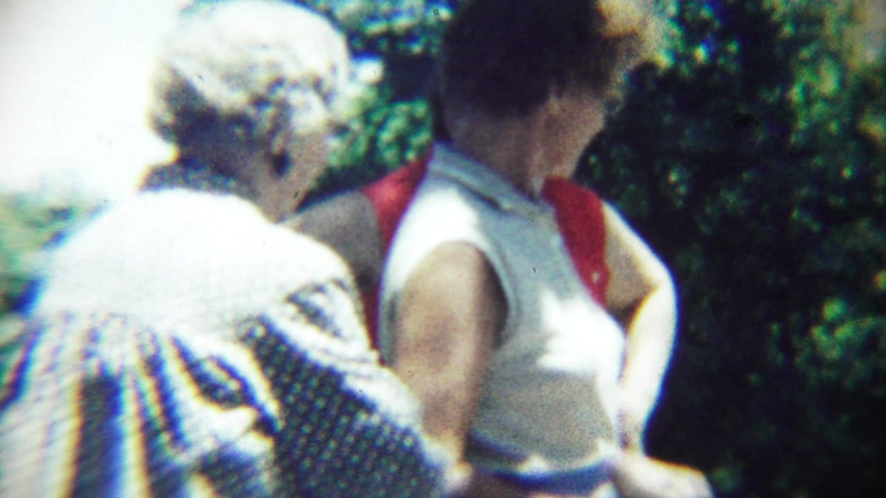 Two elderly women seated outdoors at a picnic, one in a patterned dress and one in a white sleeveless top with red fabric.