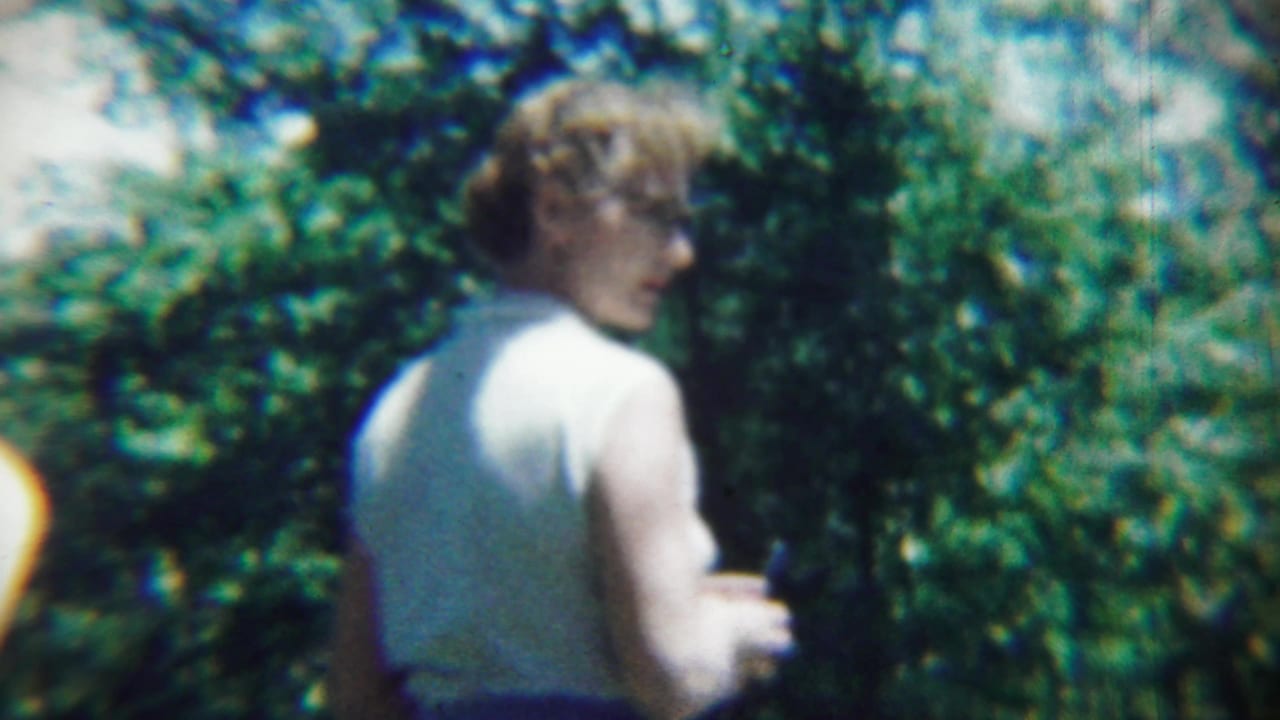 Woman in a white sleeveless top stands outdoors with trees behind her.