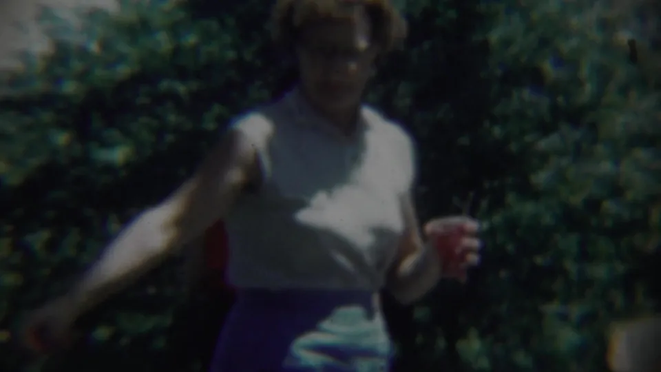 The woman appears in darker exposure as she moves through shade, holding a small red object against a leafy outdoor background.
