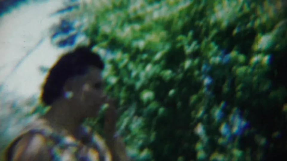 A soft-focus profile view shows the woman in a floral dress standing among leafy trees and grass in Chadron, Nebraska.