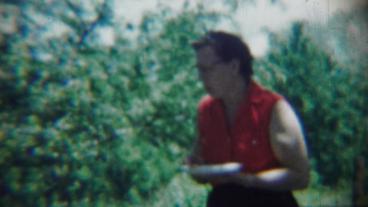 Woman in red holding a plate and looking to the side in front of foliage.