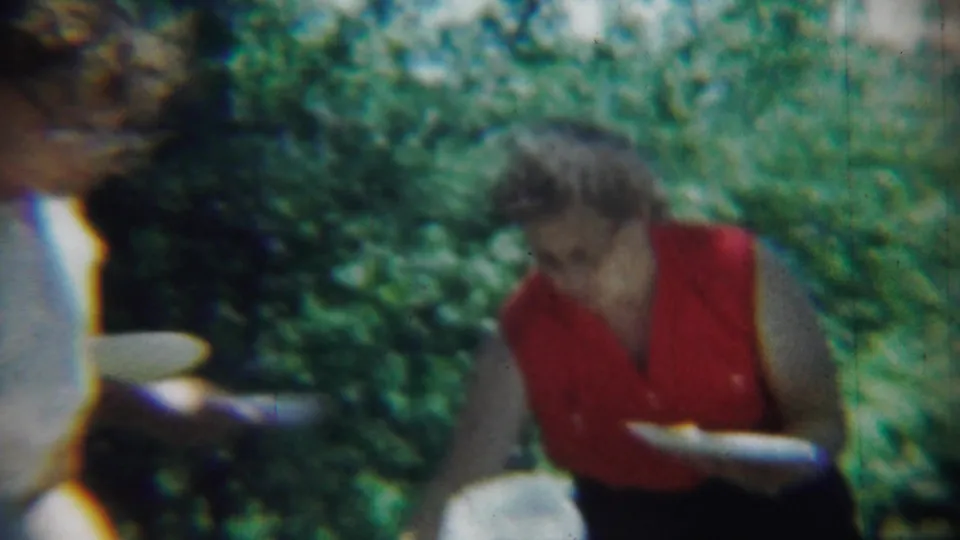 The woman in red bends or reaches with her plate while another guest is partly visible at the edge of the frame.