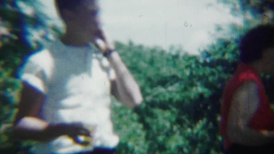 In 1959 Chadron, Nebraska home-movie footage, a young man in a white T-shirt stands outdoors near leafy trees.