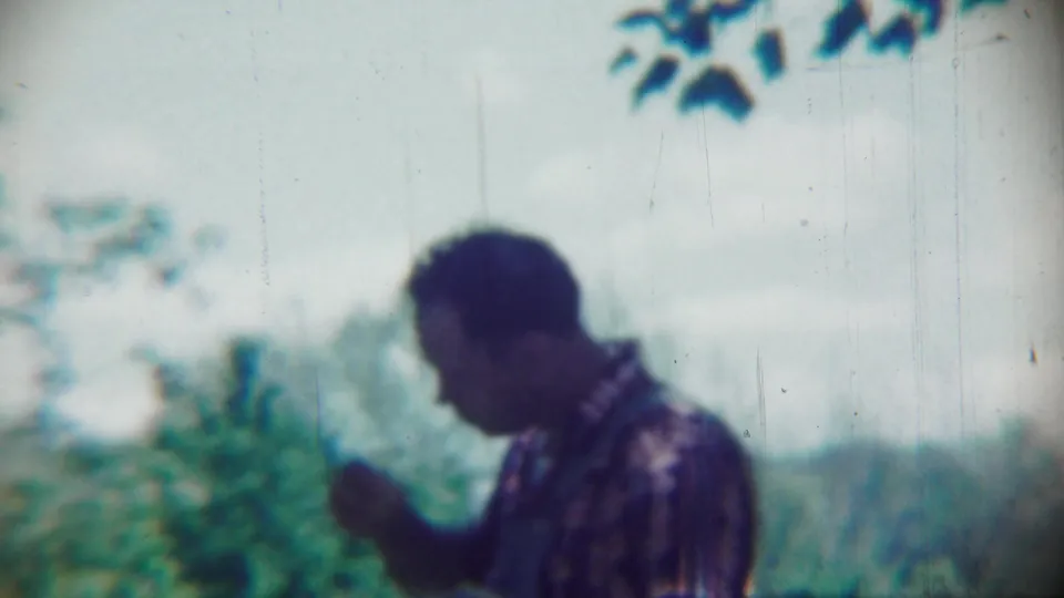 A man in a patterned shirt raises a hand in the soft, handheld 1959 Chadron, Nebraska outdoor home-movie scene.
