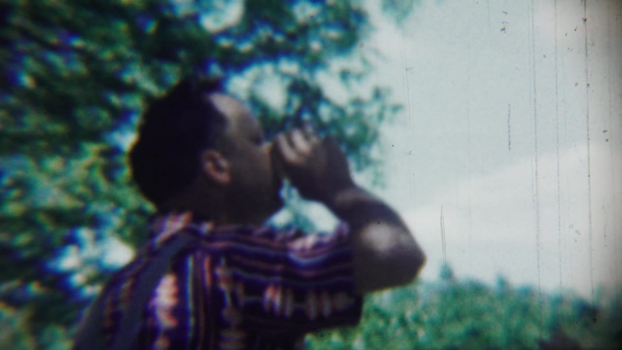 The man remains in profile with a cup raised, framed by greenery and bright sky in 1959 Chadron, Nebraska home-movie footage.