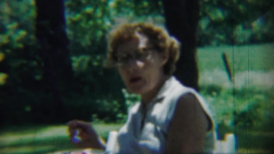 A woman in glasses appears mid-bite or mid-conversation in Chadron, Nebraska, 1959 park home-movie footage.