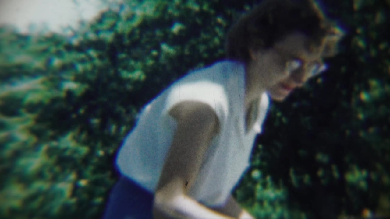 Woman with glasses smiles while moving past garden foliage.