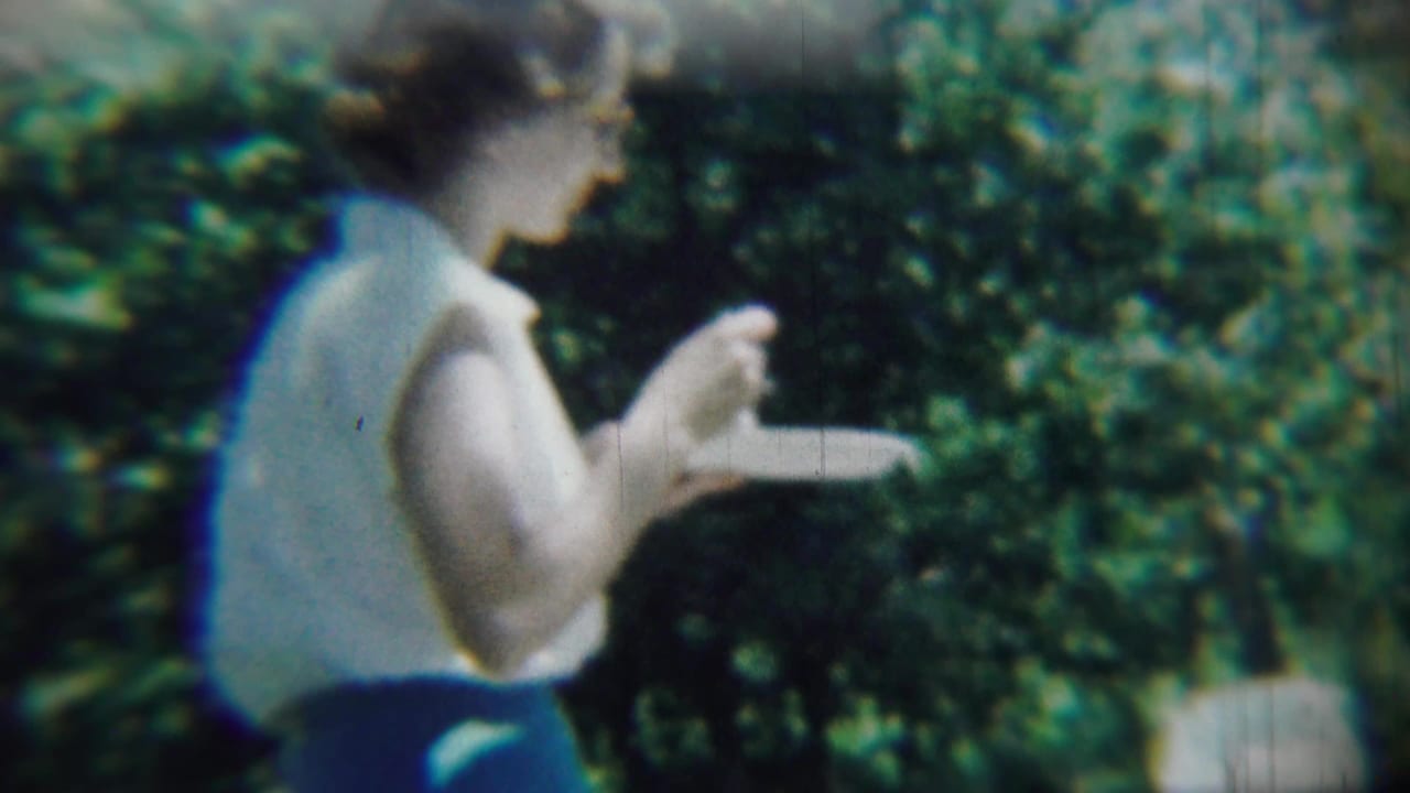 Woman in a sleeveless top eats from a paper plate beside dense greenery.