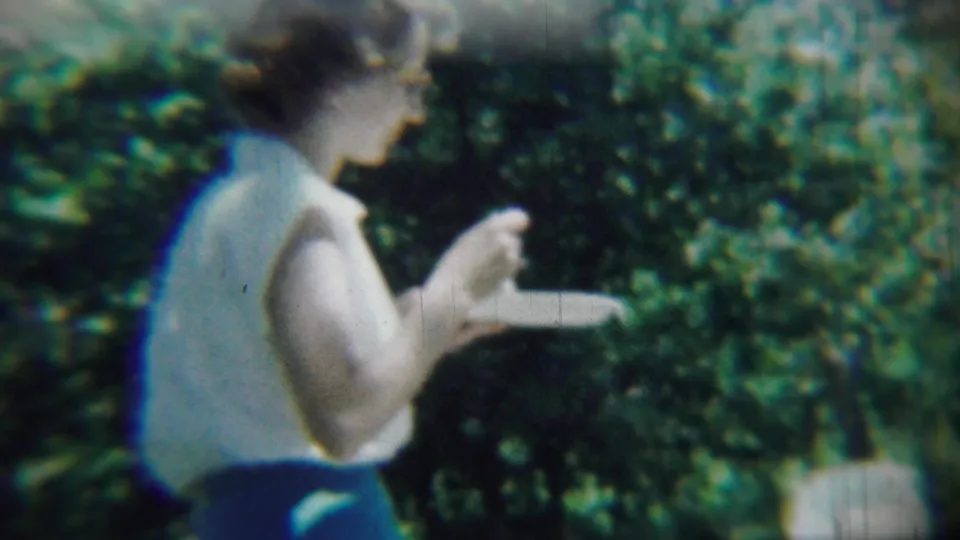 1959 Chadron, Nebraska frame of a woman in a white sleeveless top eating from a paper plate outdoors.
