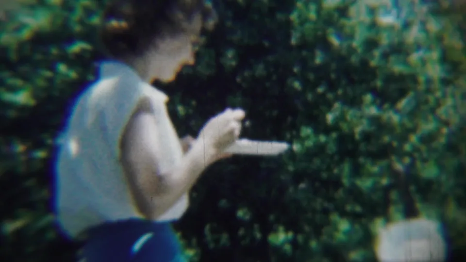 1959 Chadron, Nebraska home-movie still of a woman standing outdoors with a plate and food in hand.