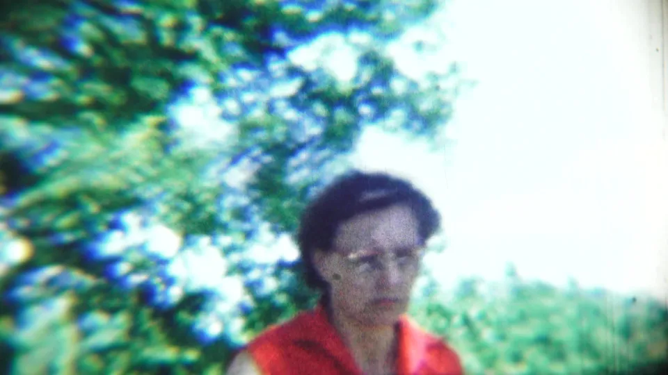 An adult woman in a red shirt faces the camera in the Chadron wooded setting, her face soft but visible in the 8mm frame.
