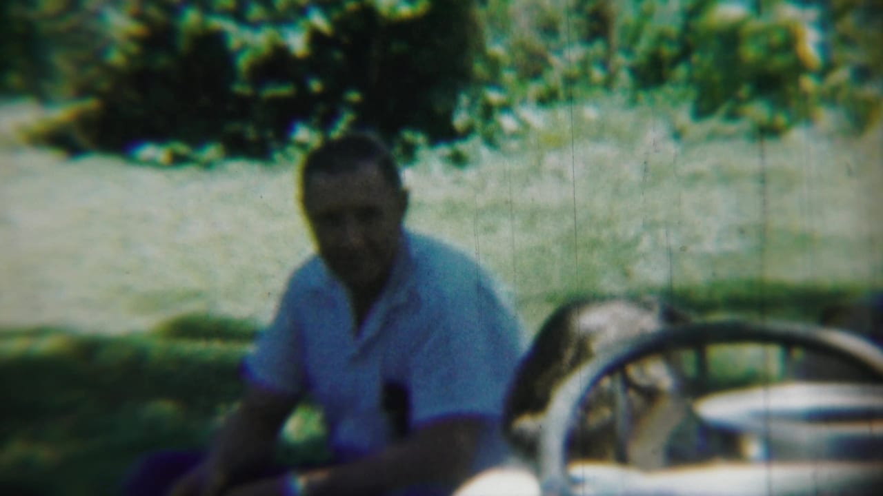 Adult man seated outdoors near a pale vintage car in Chadron, Nebraska home-movie footage from 1959.
