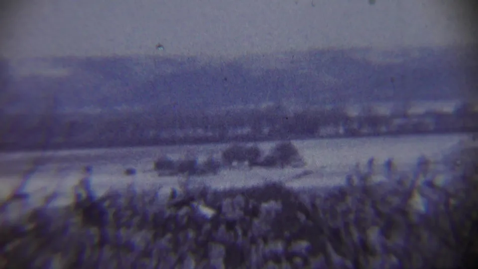 A grainy 1959 8mm frame of snowy rural ground near Chadron, Nebraska, with distant hills and dark brush in the foreground.