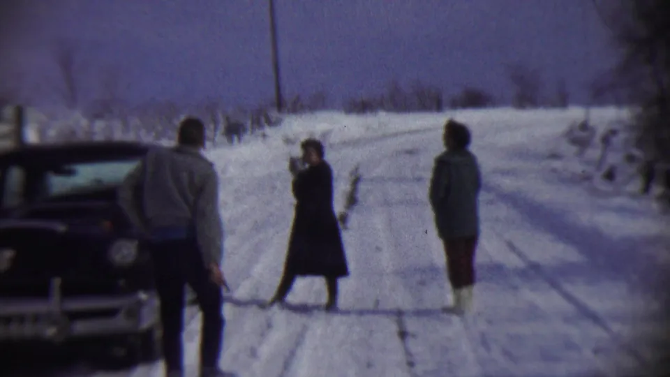 Three people in winter coats stand near a dark car on a snow-covered road in Chadron, Nebraska, in 1959 8mm home-movie footage.