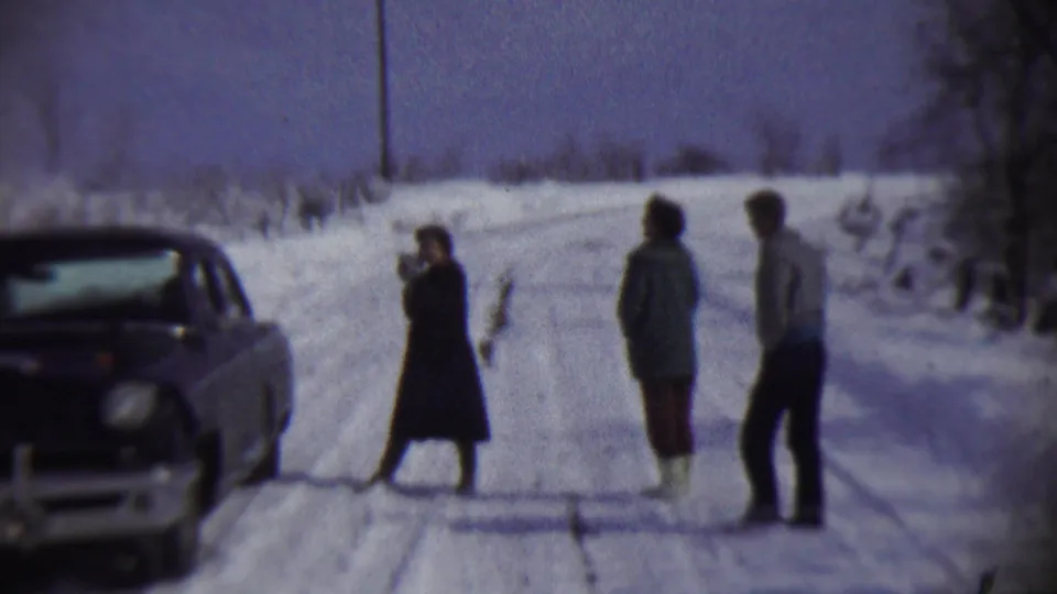 1959 Chadron, Nebraska frame showing three bundled family members on a snowy rural road, with a vintage car parked nearby.