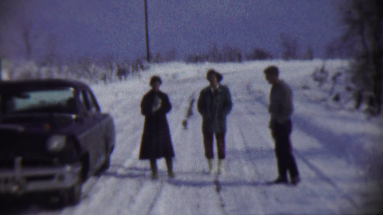 In Chadron, Nebraska in 1959, three adults stand on a snow-covered rural road near a vintage car.