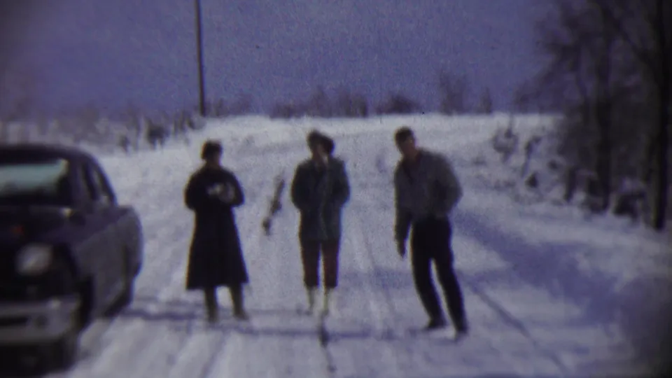 Three people in winter clothing stand on a snowy rural road in Chadron, Nebraska, with a car partly visible at left.