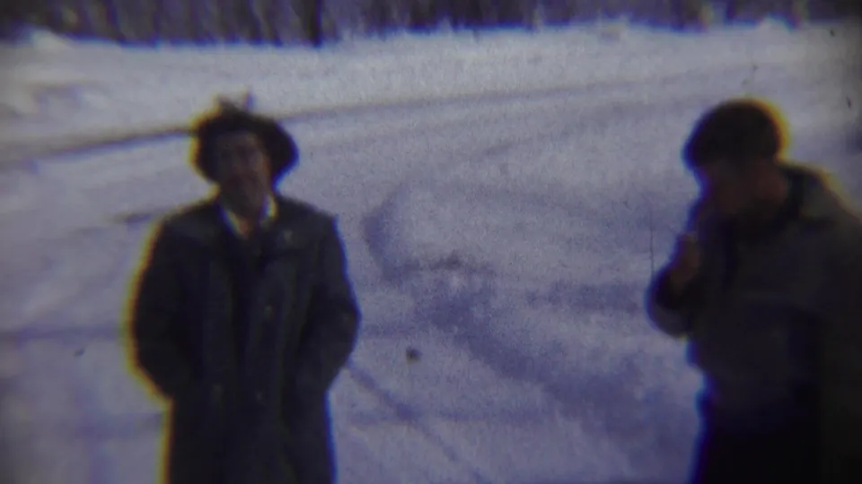 Adult man in a dark coat and brimmed hat stands outdoors in snowy Chadron, Nebraska home-movie footage from 1959.