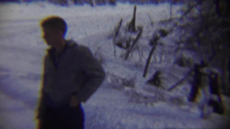 Adult man in a light jacket turns in profile amid snow and bare brush in 1959 Chadron, Nebraska home-movie footage.