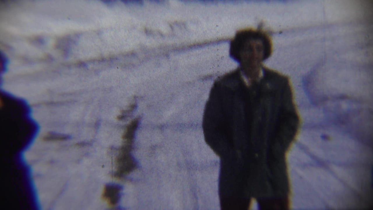 Adults in winter coats standing on a snowy street, seen in soft-focus 8mm footage.