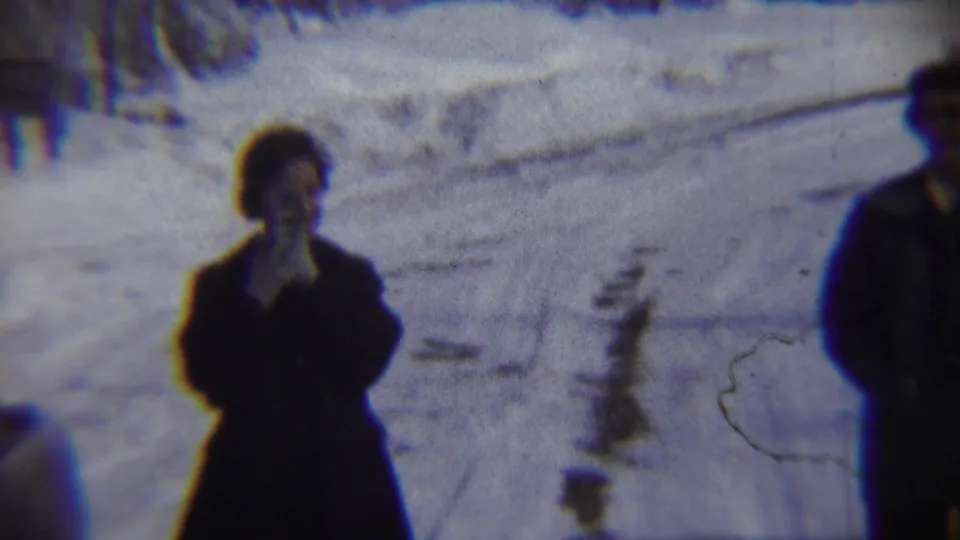 A bundled woman stands on the snowy Chadron street while a blurred foreground figure crosses the 8mm frame.