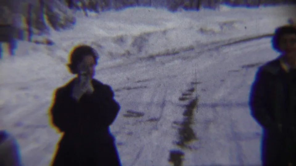 The woman remains on the snow-covered Chadron street, with another adult partly framed at the right in blue-tinted 1959 8mm footage.