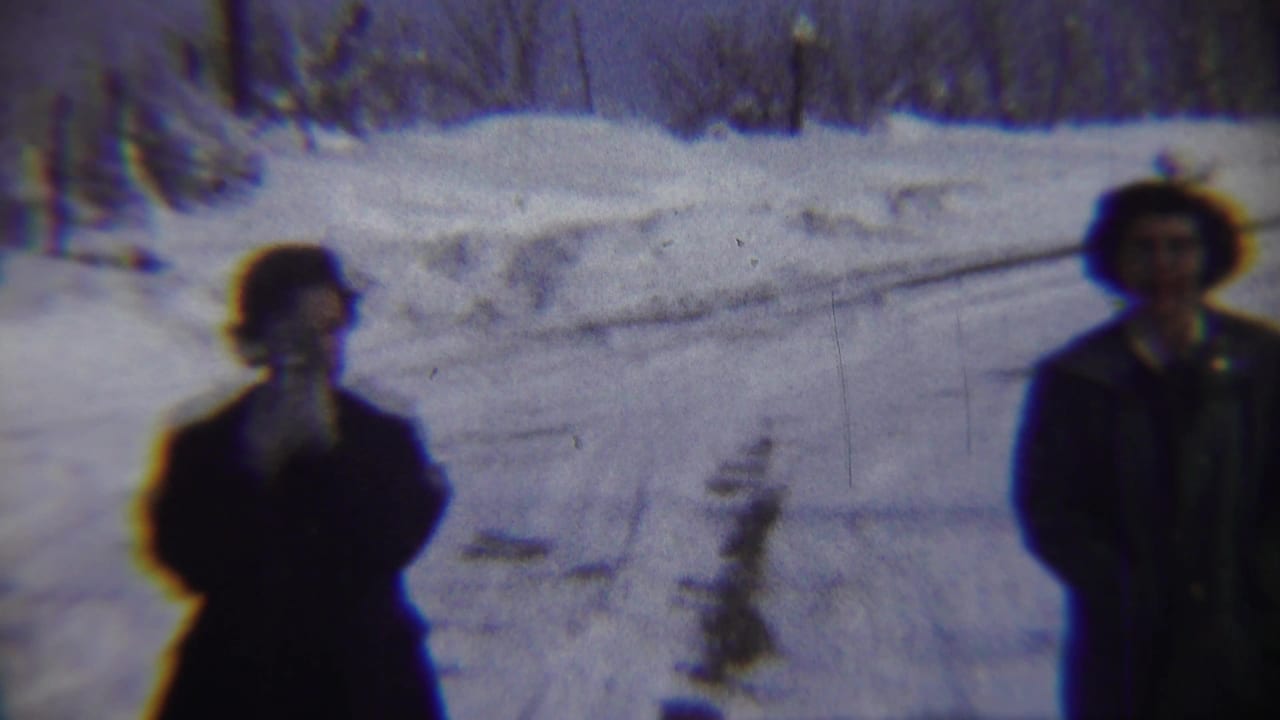 In Chadron, Nebraska 1959 home-movie footage, two adults in dark winter clothing stand amid deep snow and bare trees.