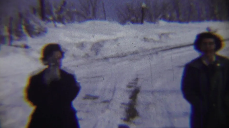 In Chadron, Nebraska 1959 home-movie footage, two adults in dark winter clothing stand amid deep snow and bare trees.