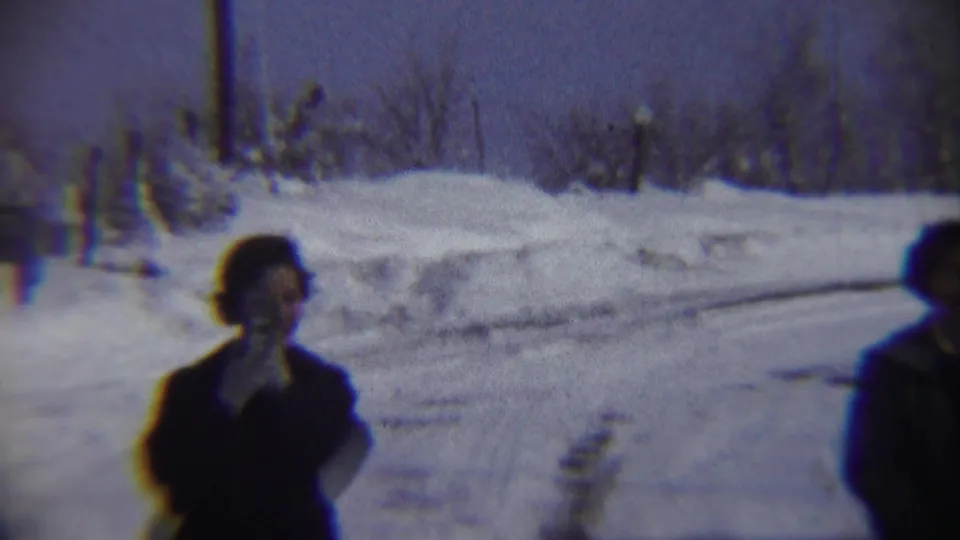 A 1959 Chadron, Nebraska winter frame shows one bundled adult in snow with another person partly cropped at the right edge.