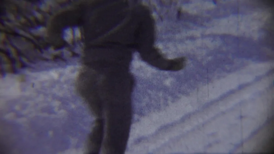 A bundled child runs close to the camera on a snow-covered road in Chadron, Nebraska, in grainy 1959 8mm footage.