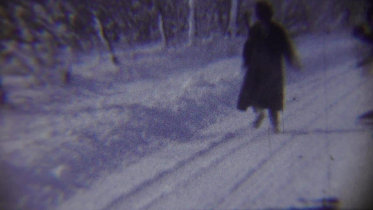 A woman in a long dark winter coat moves along a plowed snowy road in the Chadron, Nebraska home-movie scene.