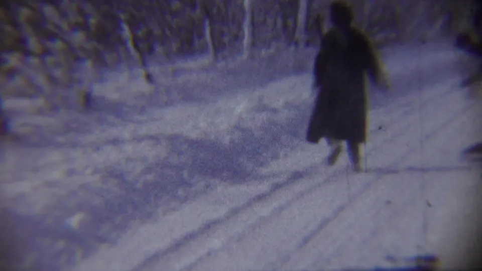 A woman in a long dark winter coat moves along a plowed snowy road in the Chadron, Nebraska home-movie scene.