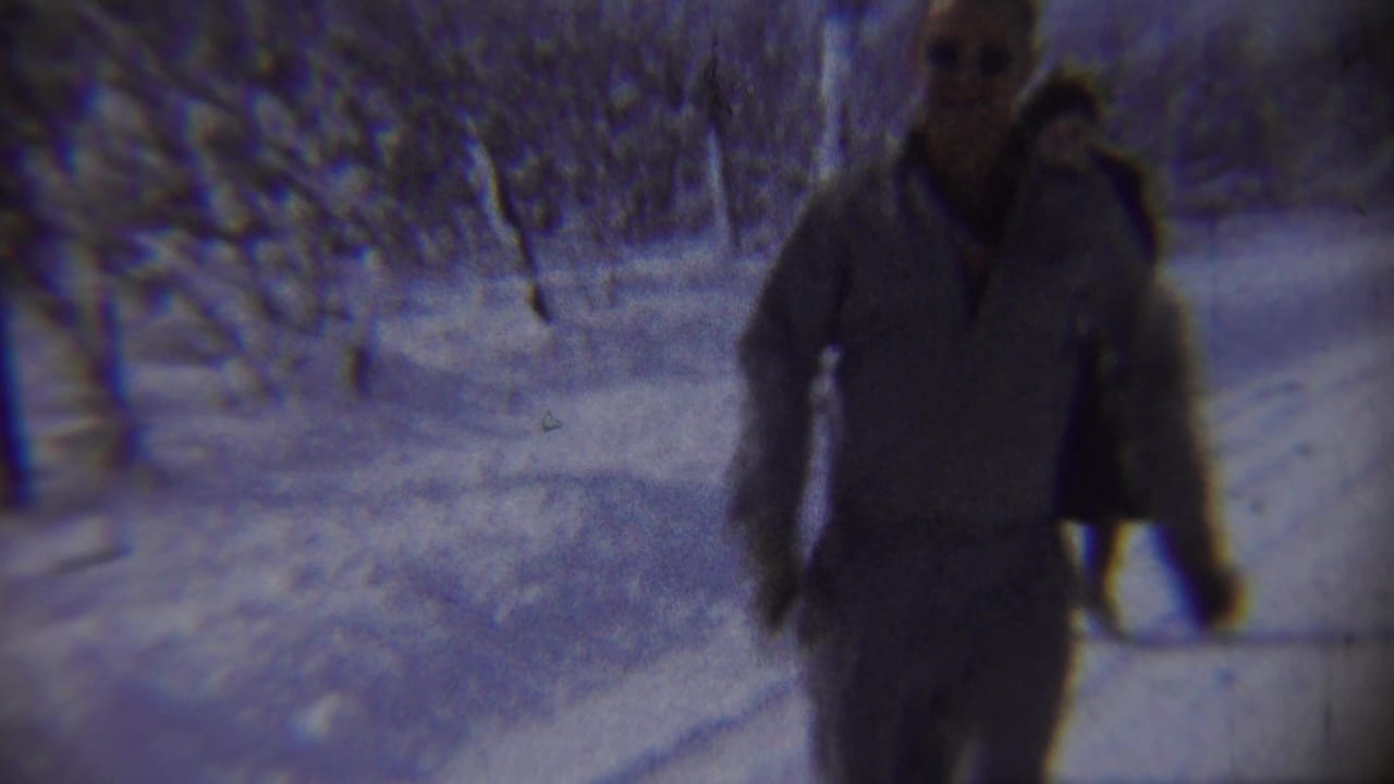 Two adults moving toward the camera on a snowy tree-lined road.