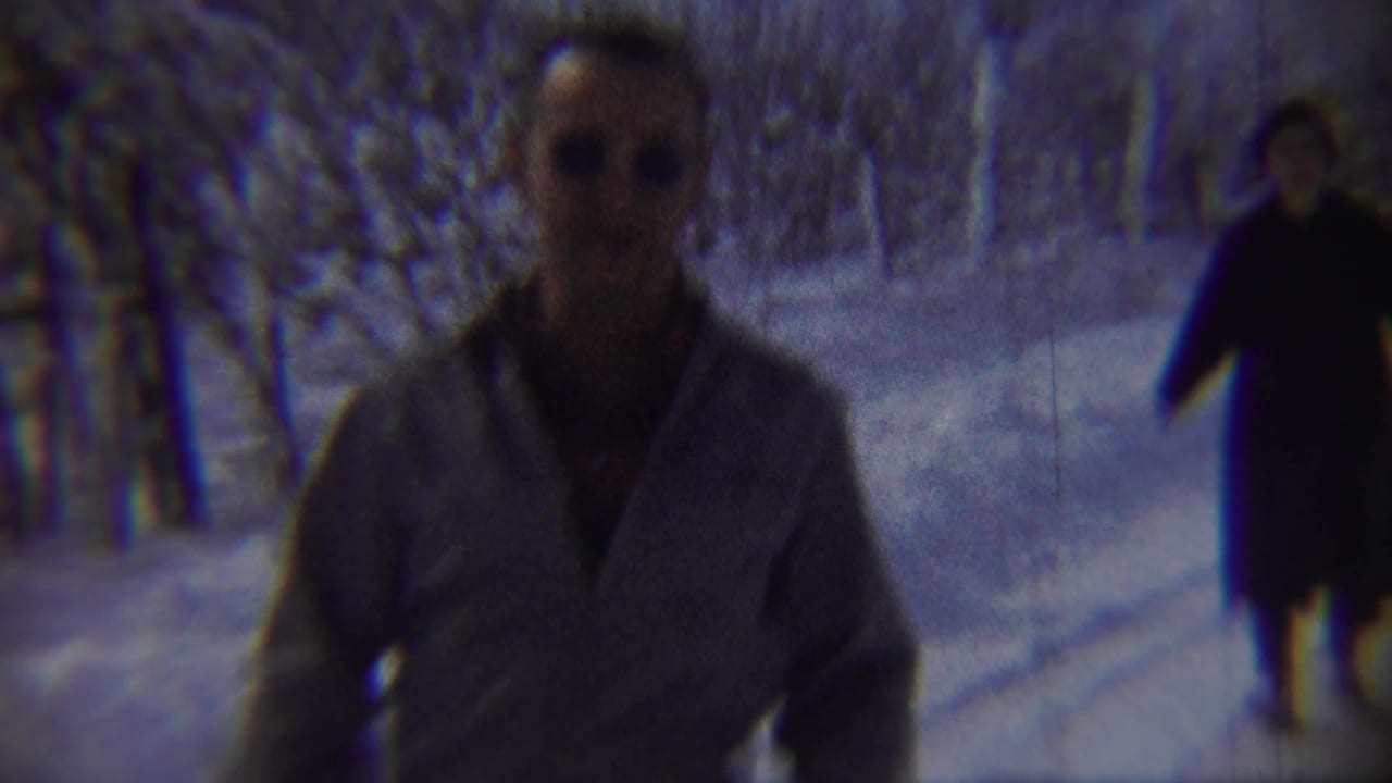 A man wearing sunglasses and a light jacket approaches close to the camera in the snowy Chadron, Nebraska scene.
