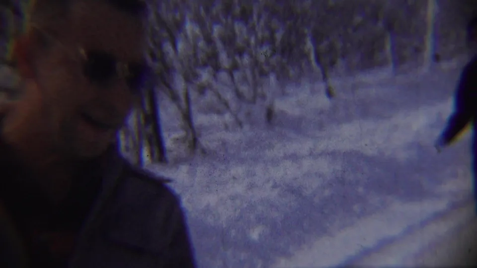 A close blurred home-movie frame shows an adult passing the camera with snow and trees in the background.