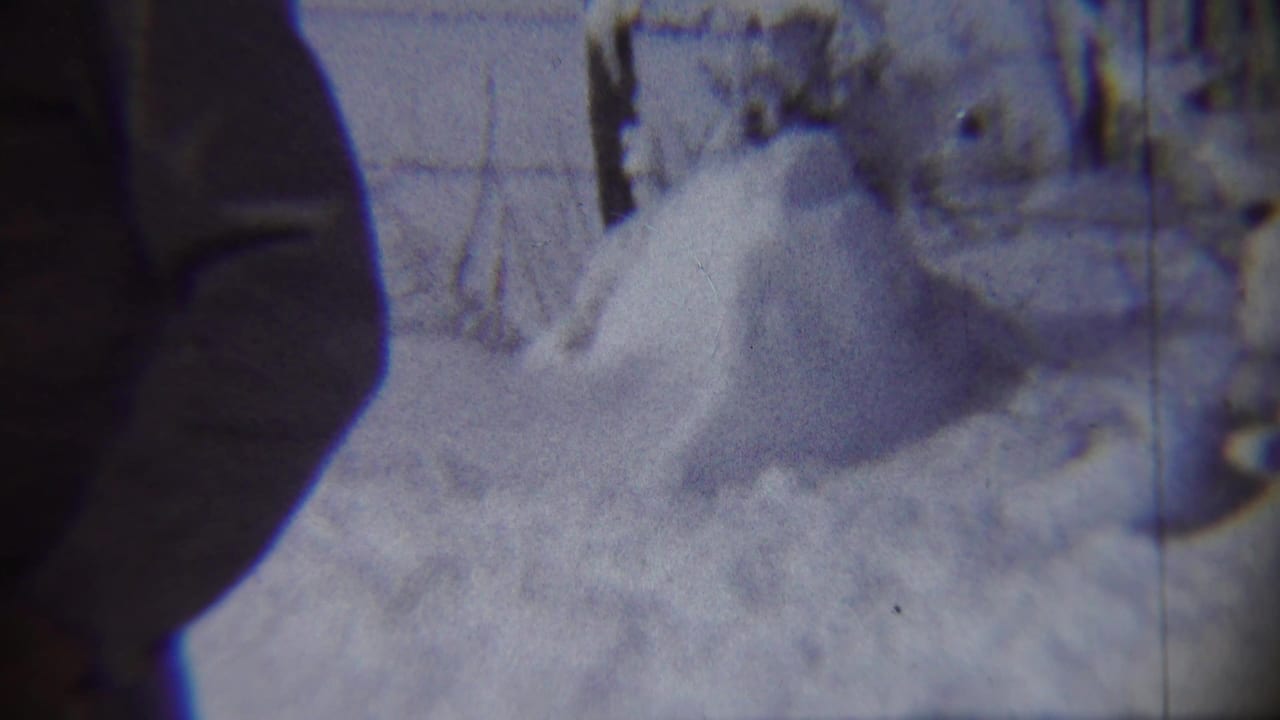 1959 Chadron, Nebraska home-movie frame showing a snowy yard and high drift, with a dark out-of-focus edge shape partly obscuring the view.