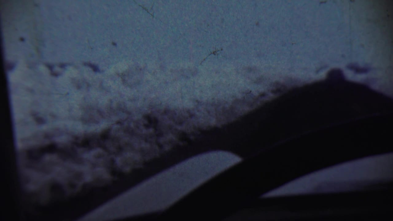 Snowy ridge seen through a dark vehicle windshield with wiper shapes in the foreground.