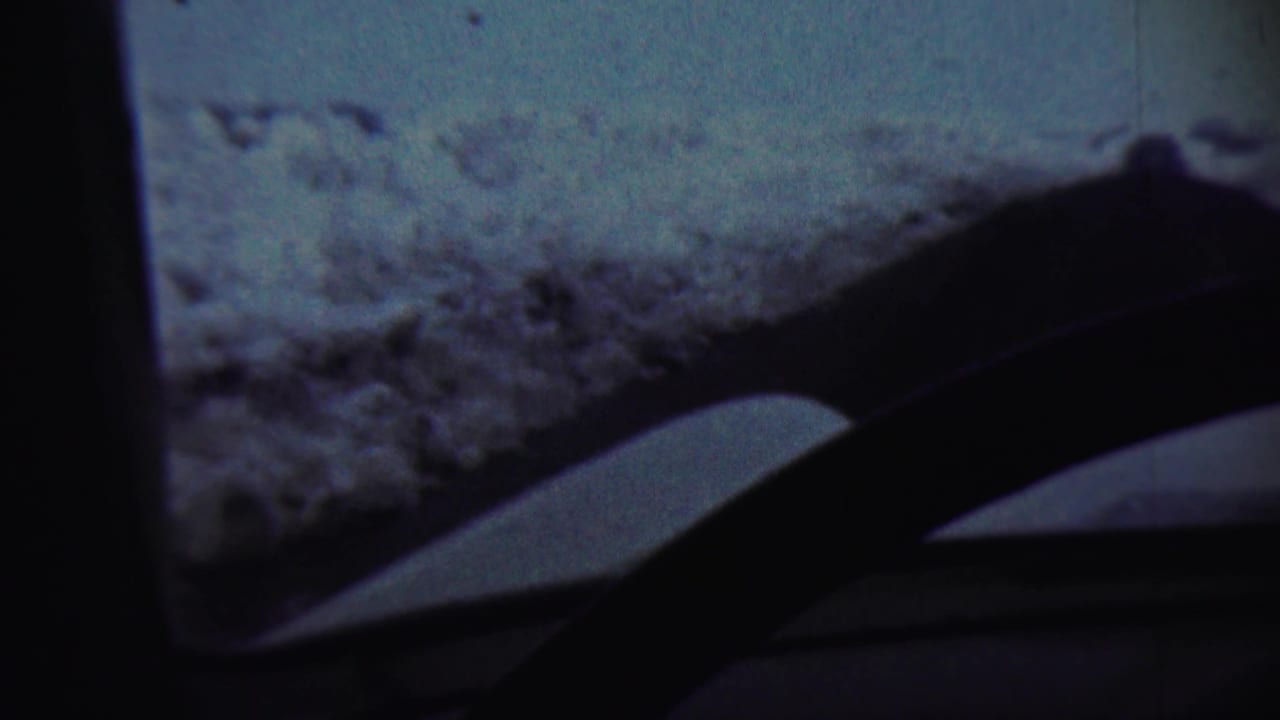 A 1959 in-car winter view near Chadron, Nebraska, with windshield wipers silhouetted against a snowy ridge and pale sky.