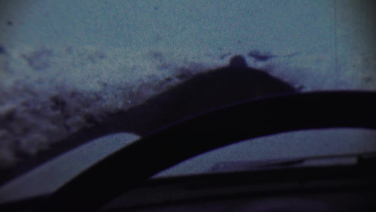 Cool-toned 8mm frame from Chadron, Nebraska, with snow outside the vehicle and a dark interior edge across the lower view.