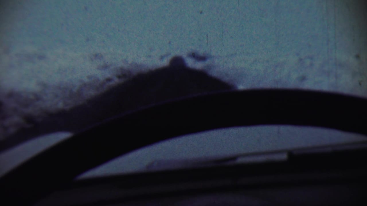 Snowy slope seen through a car windshield with a dark dashboard edge and wiper silhouette.