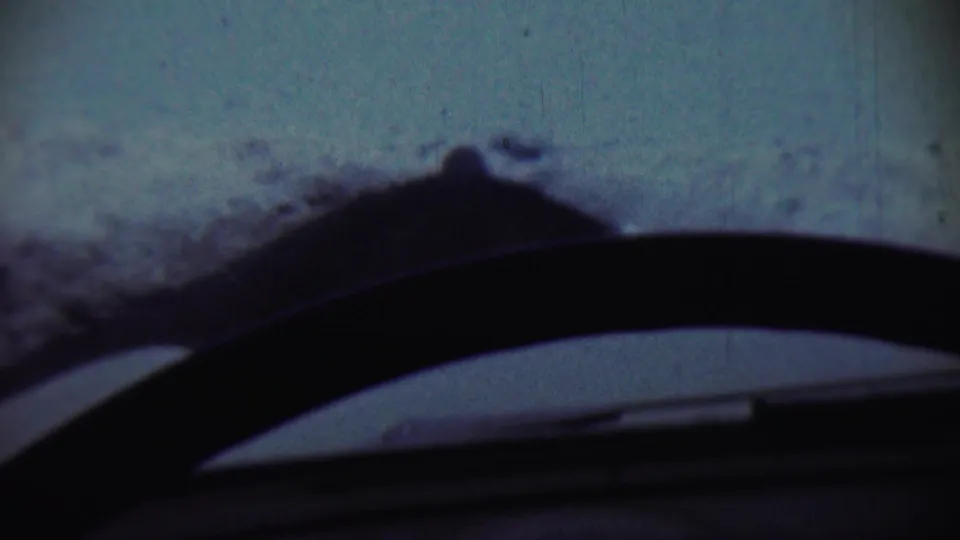 1959 Chadron, Nebraska home-movie frame showing snow-covered terrain through a windshield with the car interior silhouetted below.