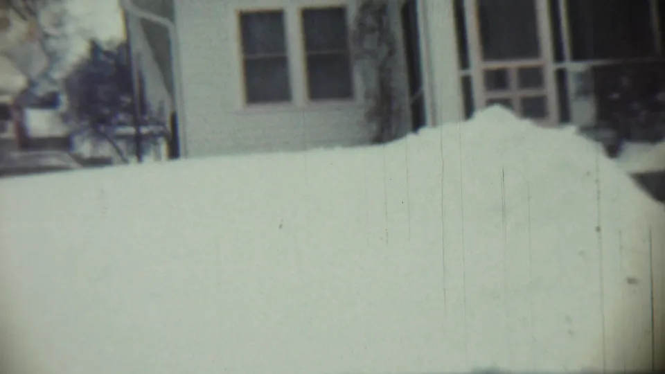 1959 Chadron, Nebraska frame with a modest house, porch rail, shrubs, and deep snowdrifts in front.