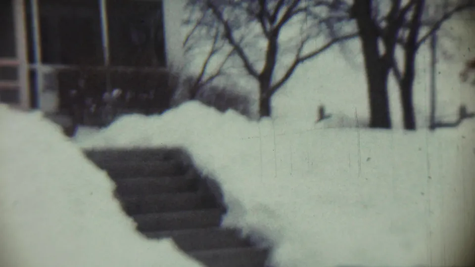 A late-1950s Chadron home exterior appears through soft 8mm focus, with front steps, deep snow, and a leafless tree.