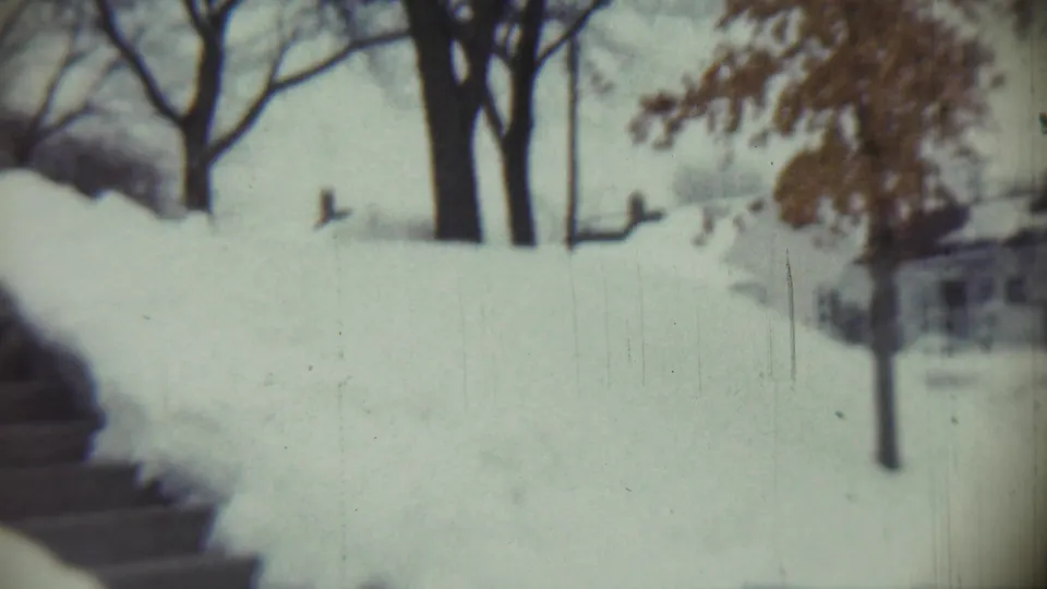 Deep snow surrounds a yard and steps in Chadron, Nebraska, with leafless trees visible through soft 8mm focus.