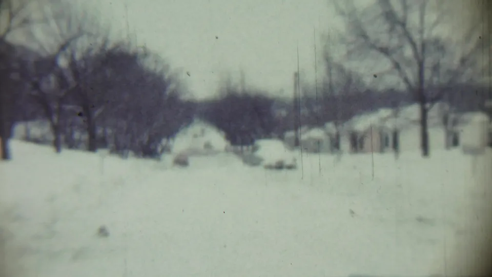 Soft 8mm frame of a Chadron, Nebraska residential area in 1959, with deep snow, bare trees, and houses set back from the road.