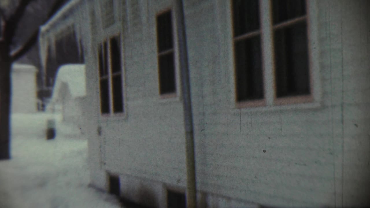 Snow beside a white wooden house with windows and a downspout.