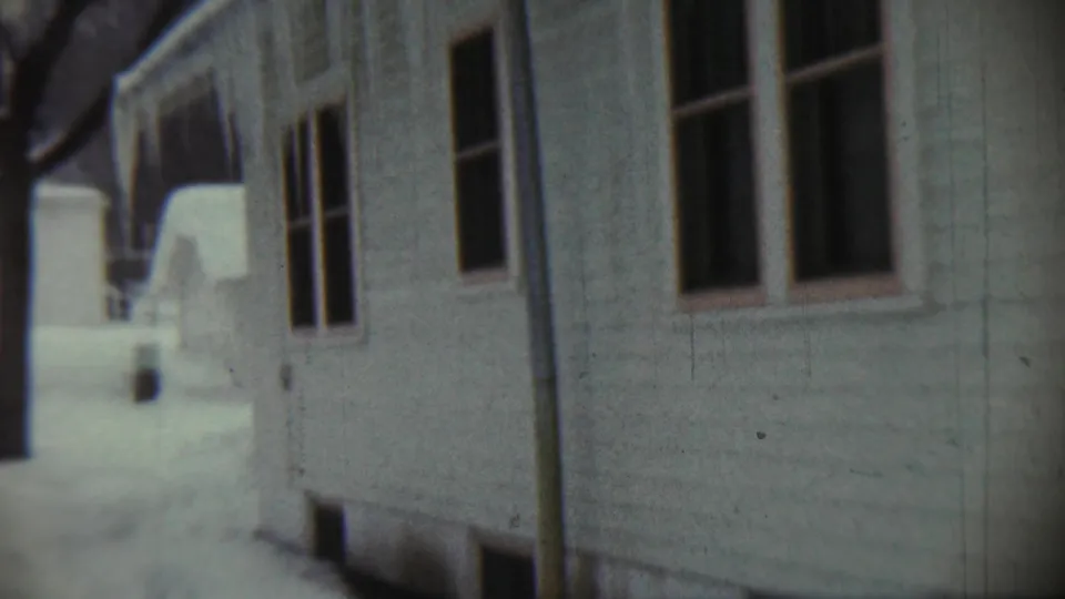 1959 Chadron, Nebraska home-movie frame showing a snowy white house exterior with dark windows and a vertical downspout.