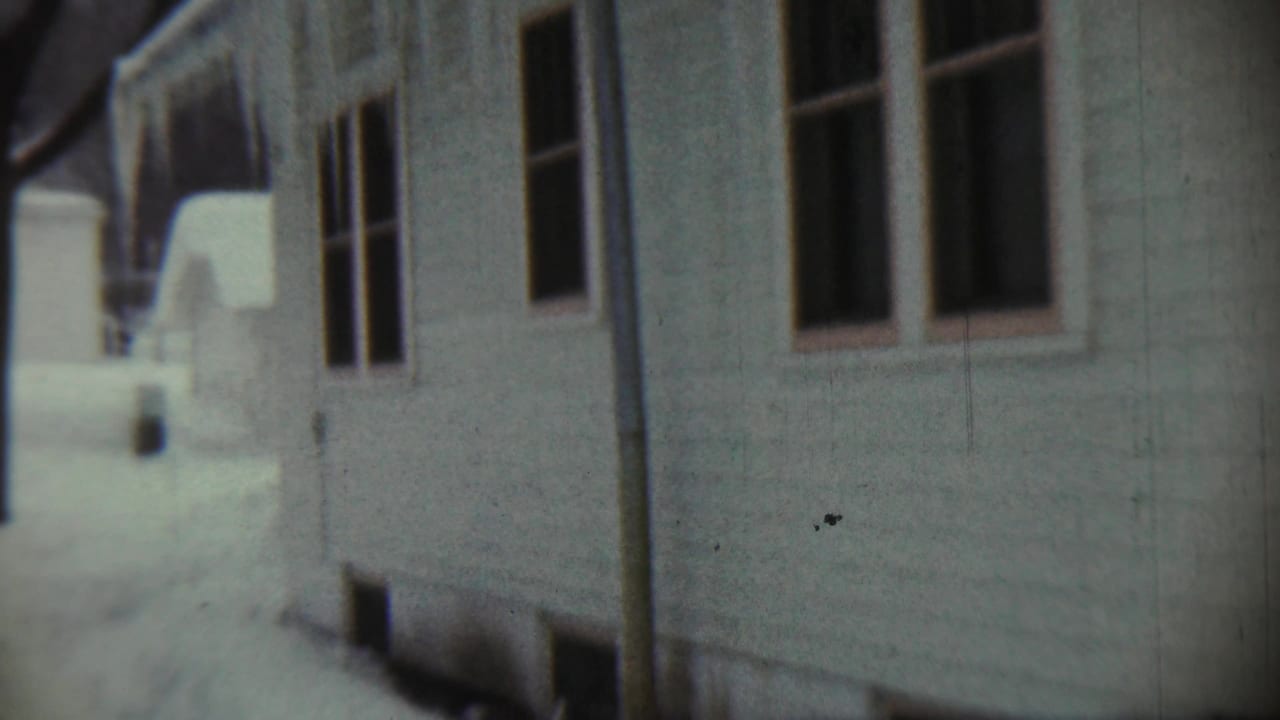 1959 Chadron, Nebraska frame with a close handheld view of white siding, dark window frames, and snow along the house.