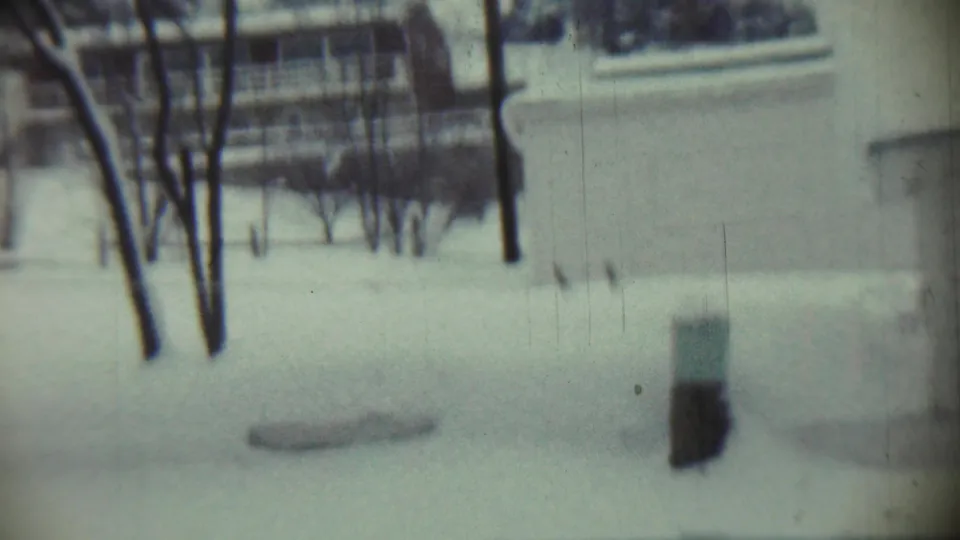 1959 Chadron, Nebraska 8mm frame of a snow-covered backyard area with bare trees and a residential wall at the right.